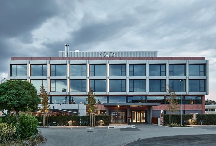 Gebäudefront mit Eingang und Vorplatz bei bewölktem Himmel