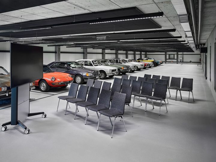 Bestuhlte Halle mit Bildschirm und mehreren Fahrzeugen