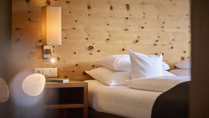Bett mit weißer Wäsche vor heller Holzwand