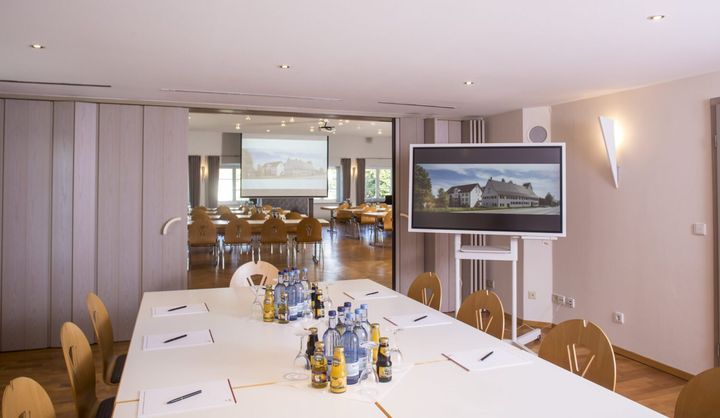 Tagungsraum mit langen Tischen und Bildschirm an der Wand