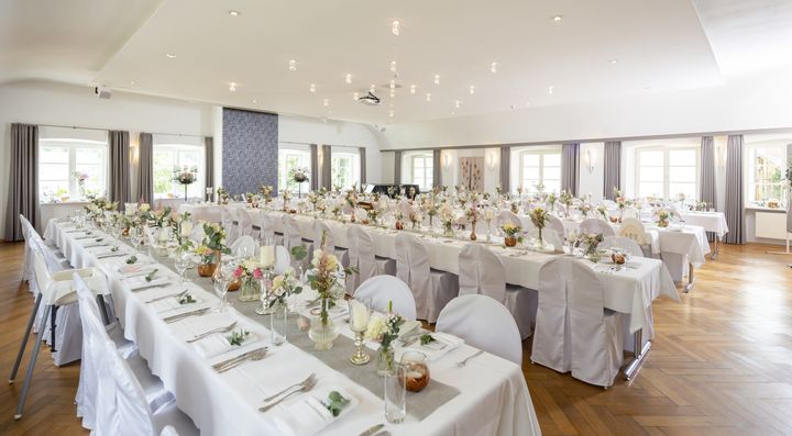 Langer festlich gedeckter Tisch mit Blumenschmuck im hellen Saal