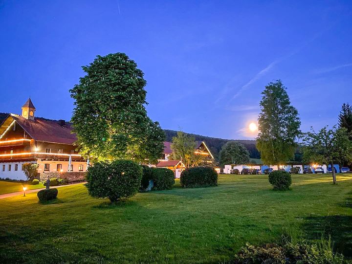 Hotel Gut Schmelmerhof mit beleuchteter Fassade, großem Baum und Vollmond am Abendhimmel