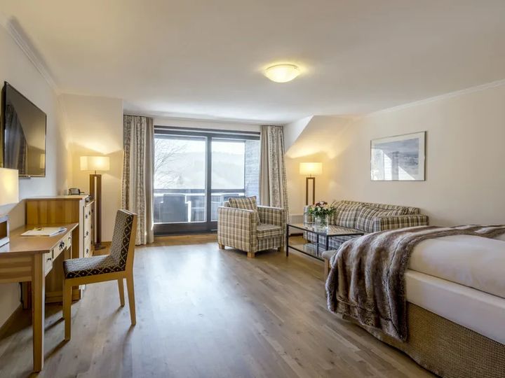 Zimmer mit Schreibtisch, Sitzgruppe und Zugang zum Balkon