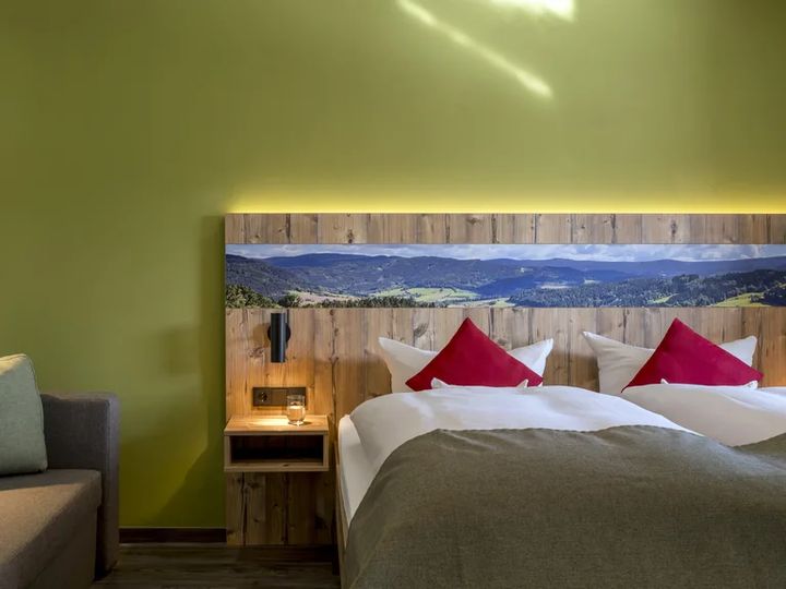 Doppelbett mit roten Kissen und Landschaftsmotiv am Kopfteil