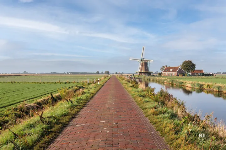 KI-Symbolbild: Klinkerstraße am Kanal in Ostfriesland mit Windmühle und Backsteinhof