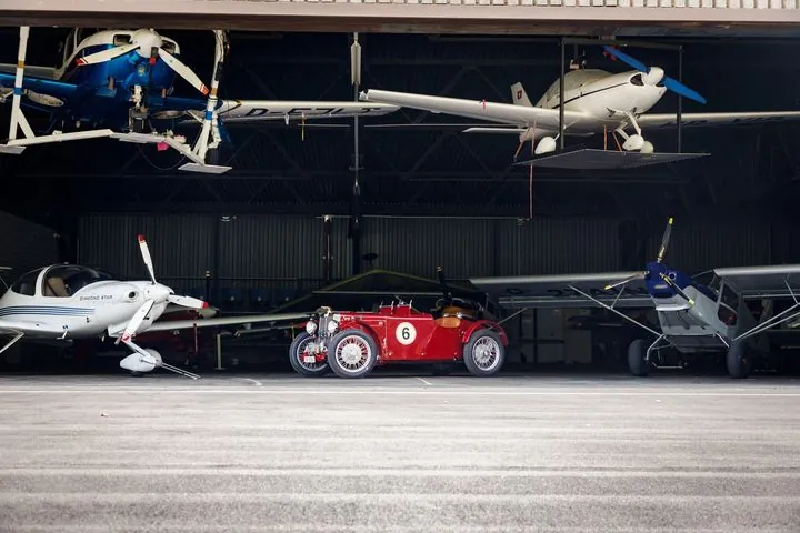 Roter Oldtimer im Hangar zwischen kleinen Flugzeugen