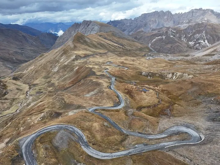 Luftbild einer kurvigen Passstraße am Col du Galibier zwischen braunen Almhängen und Felsgipfeln