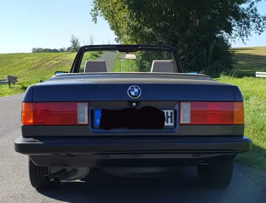 Bmw 320i Baujahr 1990 zu verkaufen – Schwarzer BMW 320i Cabrio von hinten auf einer Landstraße, Verdeck offen, rote Rückleuchten und deutsches Kennzeichen sichtbar.