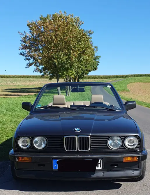 BMW 320i Baujahr 1990 zu verkaufen: Schwarzes BMW 320i E30 Cabrio von vorne mit offenem Verdeck auf einer schmalen Landstraße
