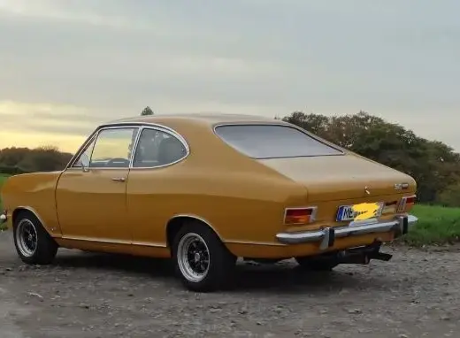 Opel Kadett B F Coupé Baujahr 1972 zu verkaufen – Goldenes Opel Kadett B F Coupé von der Seite auf Schotterweg vor grüner Wiese und Bäumen bei Sonnenuntergang.