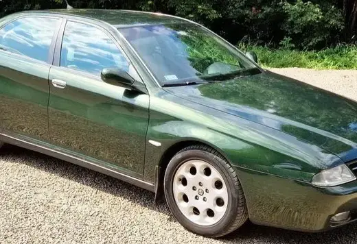 Alfa Romeo 166 Baujahr 1998 zu verkaufen, grüne Limousine schräg von vorne rechts, geparkt auf Kies vor Büschen.