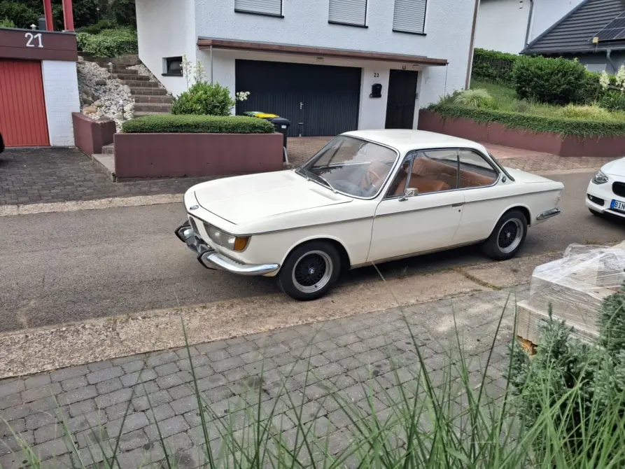BMW 2000 CS zu verkaufen, Weißer BMW 2000 CS in Seitenansicht auf gepflasterter Auffahrt geparkt, klassisches Coupé mit braunem Lederinterieur sichtbar.