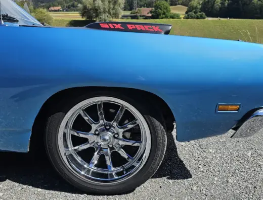 Dodge Coronet Super Bee Baujahr 1969 zu verkaufen, Vorderer Kotflügel des blauen Dodge Coronet Super Bee Coupés mit verchromter Felge, auf der Motorhaube eine Hutze mit Six-Pack-Schriftzug, Wiese im Hintergrund.