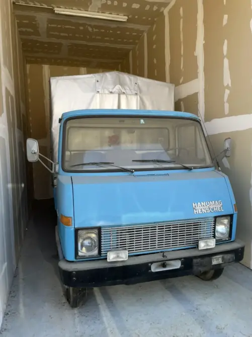 Hanomag Henschel zu verkaufen, Blauer Hanomag Henschel Lastwagen in einer Garage, Frontansicht mit charakteristischem Kühlergrill und vier Scheinwerfern.