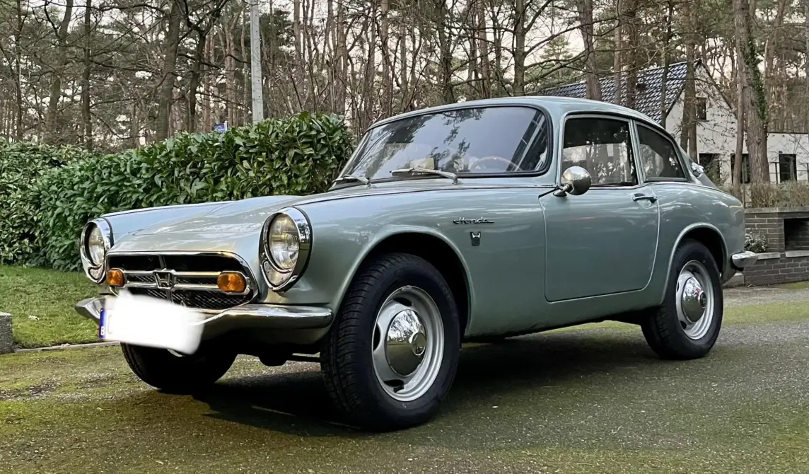 Honda S800 Baujahr 1967 zu verkaufen, Silberner Honda S800 Coupé, Dreiviertelansicht von vorn links, vor Hecke und Bäumen