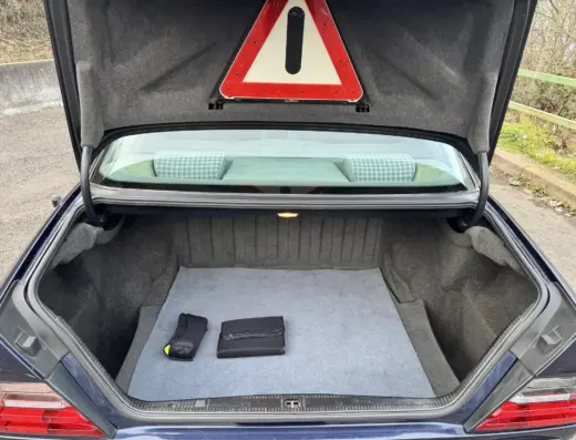 Mercedes Benz E280 Baujahr 1995 zu verkaufen – Offener Kofferraum der dunkelblauen Mercedes-Benz E280 Limousine mit grauem Teppich und Warndreieck im Kofferraumdeckel.