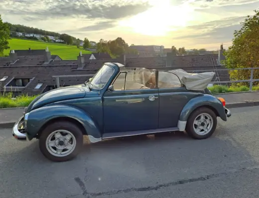 Volkswagen Käfer 1303 LS Cabriolet Baujahr 1976 zu verkaufen, Grünes Volkswagen Käfer 1303 LS Cabriolet in der Seitenansicht mit geöffnetem Verdeck und Leichtmetallrädern, im Hintergrund Hausdächer und Wiesen