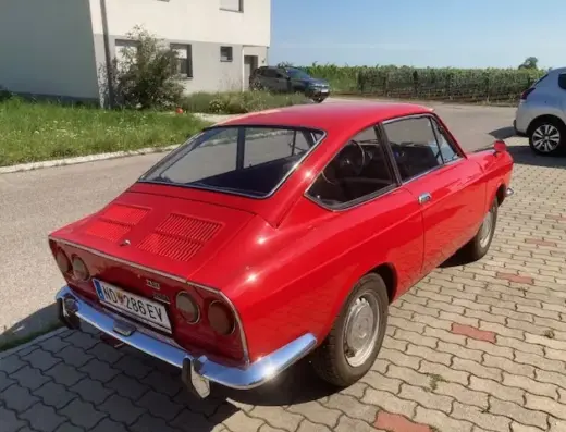 Fiat 850 Sport Coupé Baujahr 1971 zu verkaufen: Roter Fiat 850 Sport Coupé schräg von hinten auf Pflaster, Heckleuchten, Stoßstange und Nummernschild sichtbar.