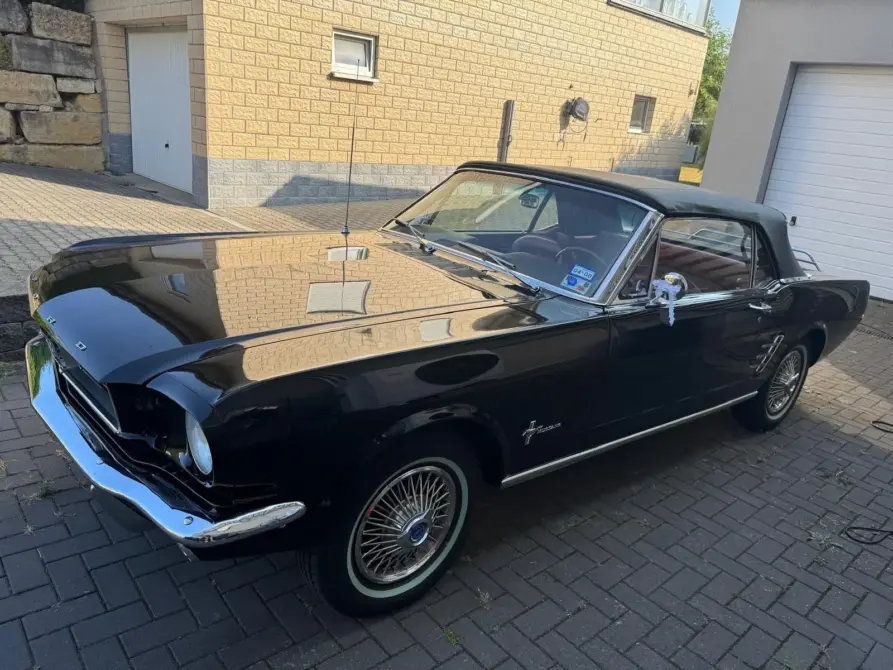 Ford Mustang Baujahr 1966 zu verkaufen: Schwarzer Ford Mustang Cabrio mit geschlossenem Verdeck schräg von vorne links auf einer gepflasterten Hofeinfahrt.