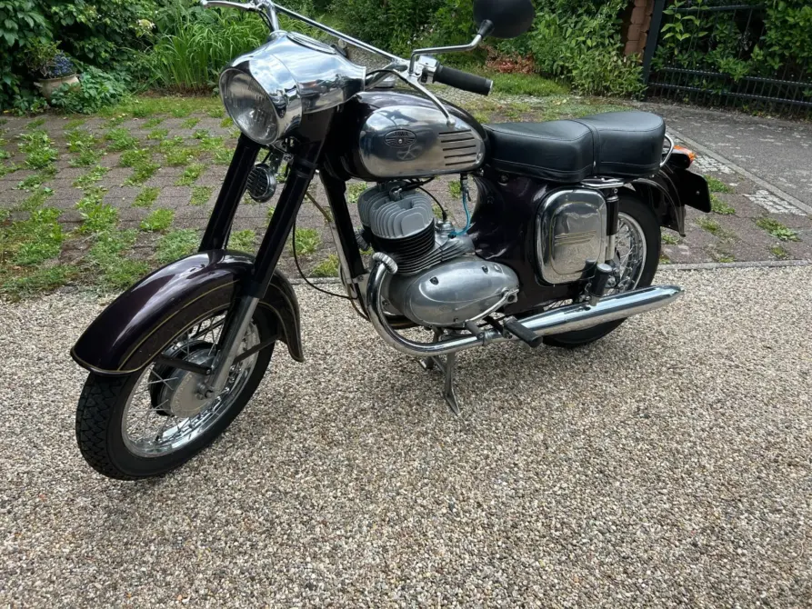 Jawa 354 Baujahr 1958 zu verkaufen: Braunes Motorrad von vorn links auf Kies, Scheinwerfer, Tank, Sitzbank, Motor, Auspuff und Kotflügel sichtbar