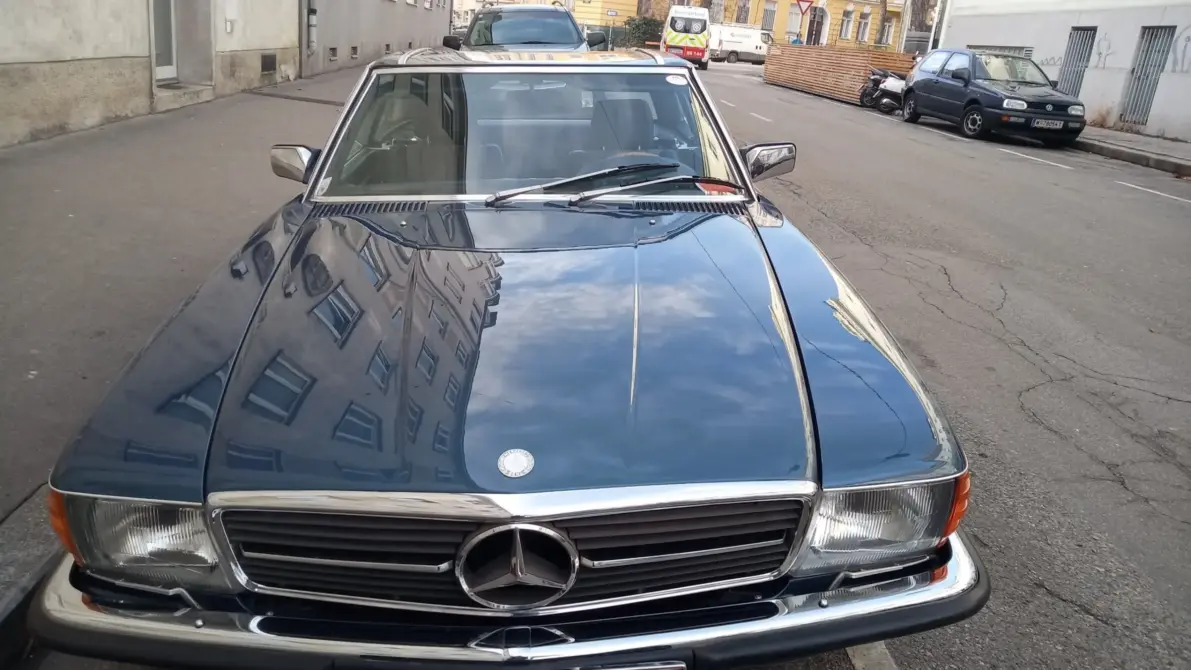 Mercedes-Benz 280 SL Baujahr 1984 zu verkaufen: Dunkelblauer Mercedes-Benz 280 SL von vorne auf Asphalt am Straßenrand, Kühlergrill, Scheinwerfer und Haube sichtbar