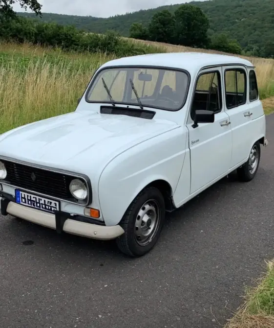 Renault 4TL Baujahr 1991 zu verkaufen: Weißer Renault 4 schräg von vorne links auf Asphalt, Wiese und bewaldete Hügel im Hintergrund