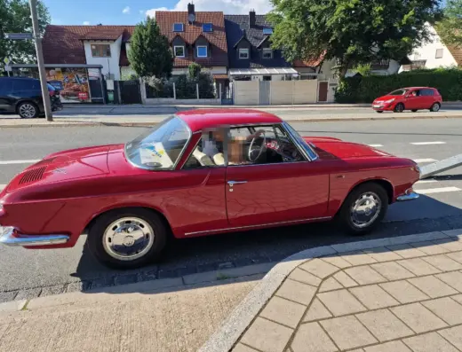 Volkswagen Karmann Ghia 1600L T34 Baujahr 1966 zu verkaufen: Roter Volkswagen Karmann Ghia 1600L T34 Coupé, Seitenansicht rechts auf einer Straße vor Wohnhäusern, Insassen unkenntlich gemacht