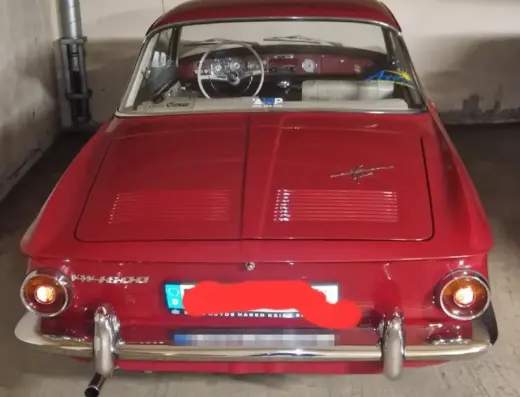 Volkswagen Karmann Ghia 1600L T34 Baujahr 1966 zu verkaufen: Heck des roten Karmann Ghia T34 in einer Tiefgarage mit Lüftungsschlitzen im Motordeckel, Rückleuchten und Schriftzug VW 1600